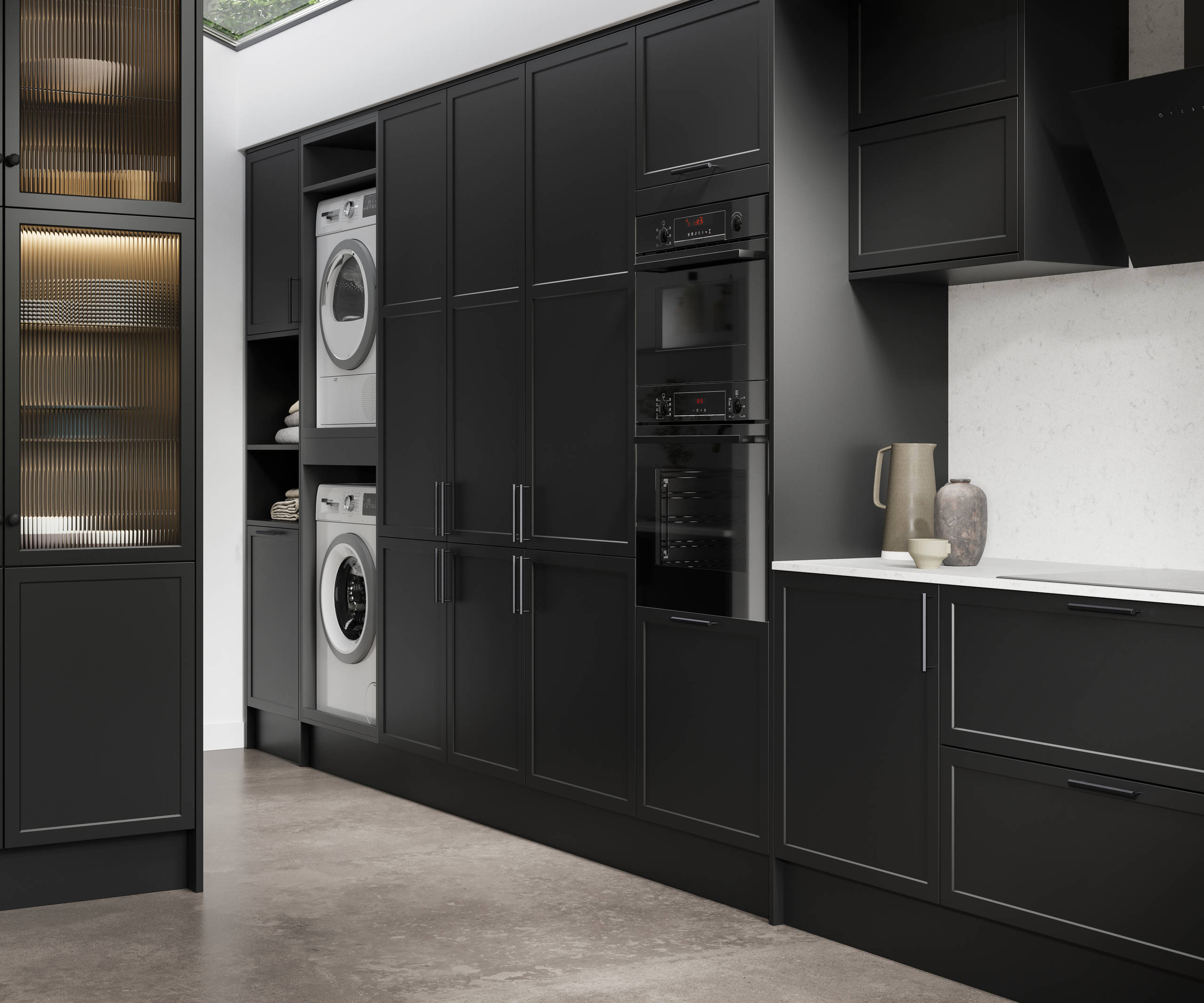 View of Modern Shaker Brunswick Sumi Black laundry room from kitchen, with integrated laundry machine and dryer as well as ovens in tall cabinetry, white worktop and splashback Silestone Miami Vena and vitrine cabinets with fluted glass doors.