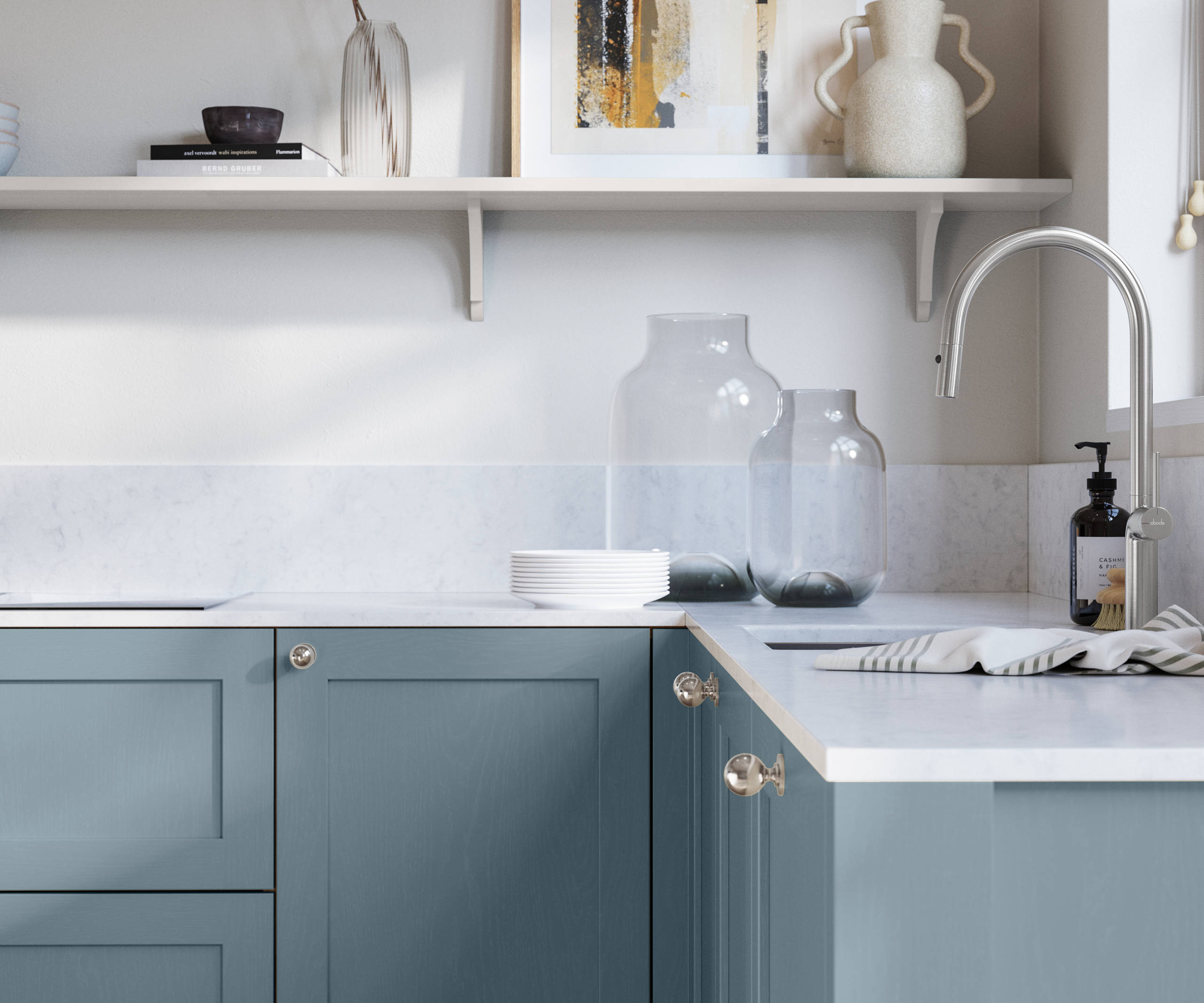 Wardley Portland Blue kitchen cabinetry with steel knobs, steel tap, white marbled worktop and matching backsplas, an open shelf on the wall above cabinets with ceramics and a vase of flowers.