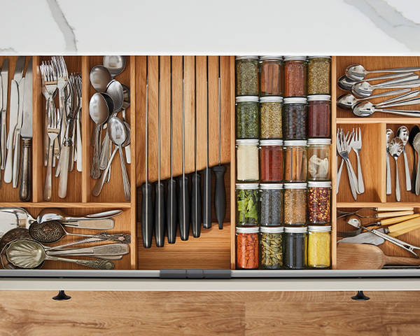 Opened drawer with oak inserts for cutlery, jars of spices and knives.