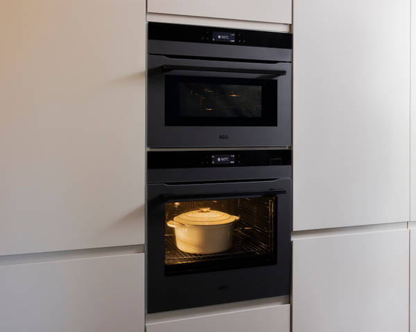 Built-in ovens in matt finish Luna cabinetry from Magnet in a neutral shade, oven turned on and containing a skillet.