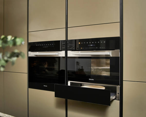 Built-in Ovens with opened warming drawer in modern slab front Balmoral Soho cabinetry from Magnet, Dekton in Ceppo worktop of kitchen island in foreground.