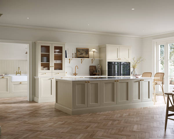 Open plan living room and Traditional Shaker-style kitchen Ludlow Parchment with tactile woodgrain, flute glass vitrine cabinets,  brass acessories like handles and tap, integrated ovens, a kitchen island and light wood herringbone flooring.