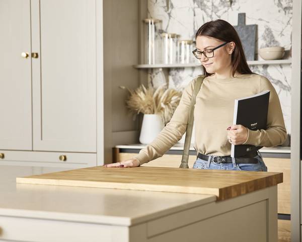 Woman holding a brochure feeling the wood worktop with her hand in a neutral shade Shaker style kitchen in a Magnet Showroom