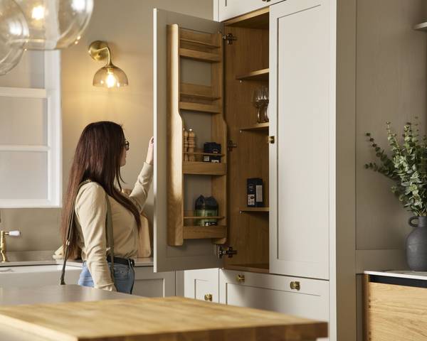 Woman looking at oak interior in larder cabinet in a showroom neutral shade Shaker kitchen from Magnet.
