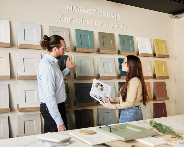 Kitchen designer pointing to front and colour samples to a woman holding an open brochure in a Magnet Showroom.