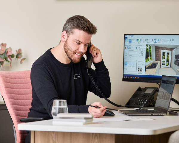 Magnet colleague at a desk, speaking on the a phone while designing a kitchen on a computer