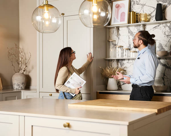 Woman holding a brochure and feeling a Shaker front with her hand while speaking to a kitchen designer in a Magnet Showroom.