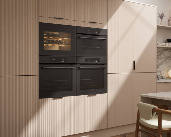 Fluted front kitchen Reed from Magnet in light warm neutral shade Shell, tall cabinets with appliances like ovens and a wine cooler, black handles
