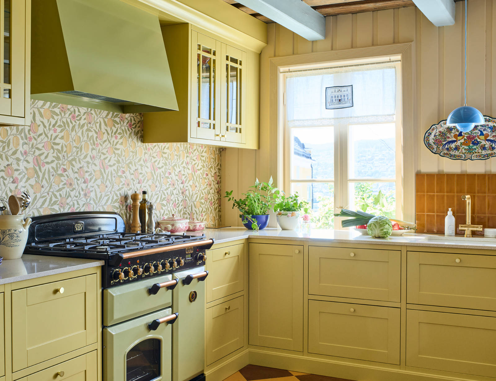 Landlig rammekjøkken Scala Inframe fra Sigdal som gir en snekkerbygged preg, vitrineskaber, Falcon Classic Olive green komfyr med gassbrennere og Røroshetta Grue ventilator i samma fargekode, messing knotter og blandebatteri