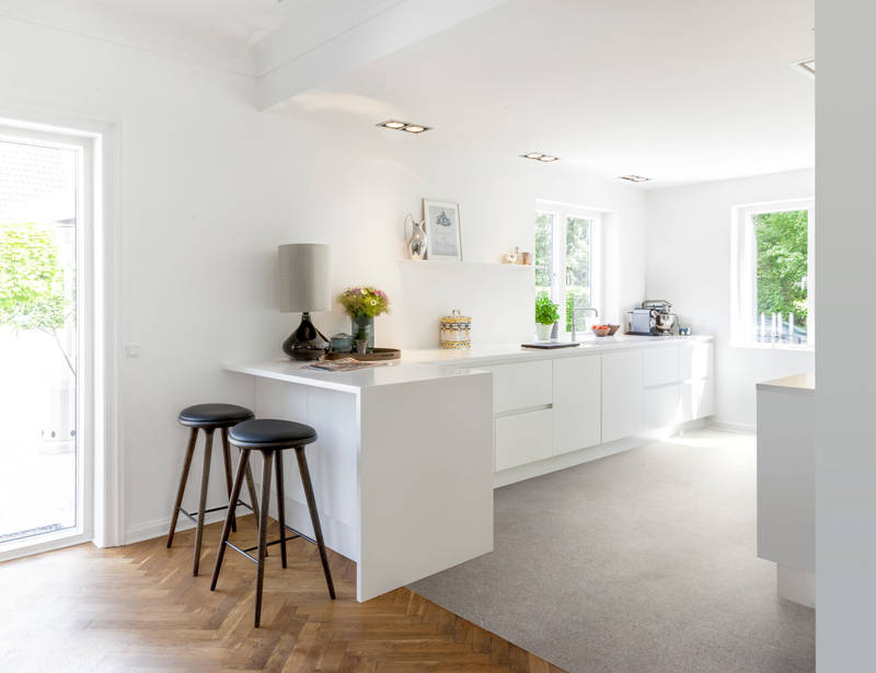 Grebsfrie hvide køkkenet Highline Frost med indfræsede greb i lågerne fra INVITA, hvid bordplade og barstole på halv køkkenø