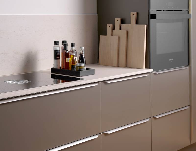 Minimalistisk brun køkken Newline Bark fra INVITA med indbygningsovne i højskabe, diskret greb i stål og lys beige bordplade med matchende splashback