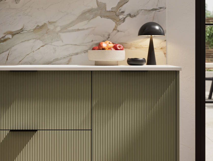 Fluted front kitchen Reed from Magnet in deep green shade Balmoral, with a marbled splashback and black handles, herringbone wood flooring.