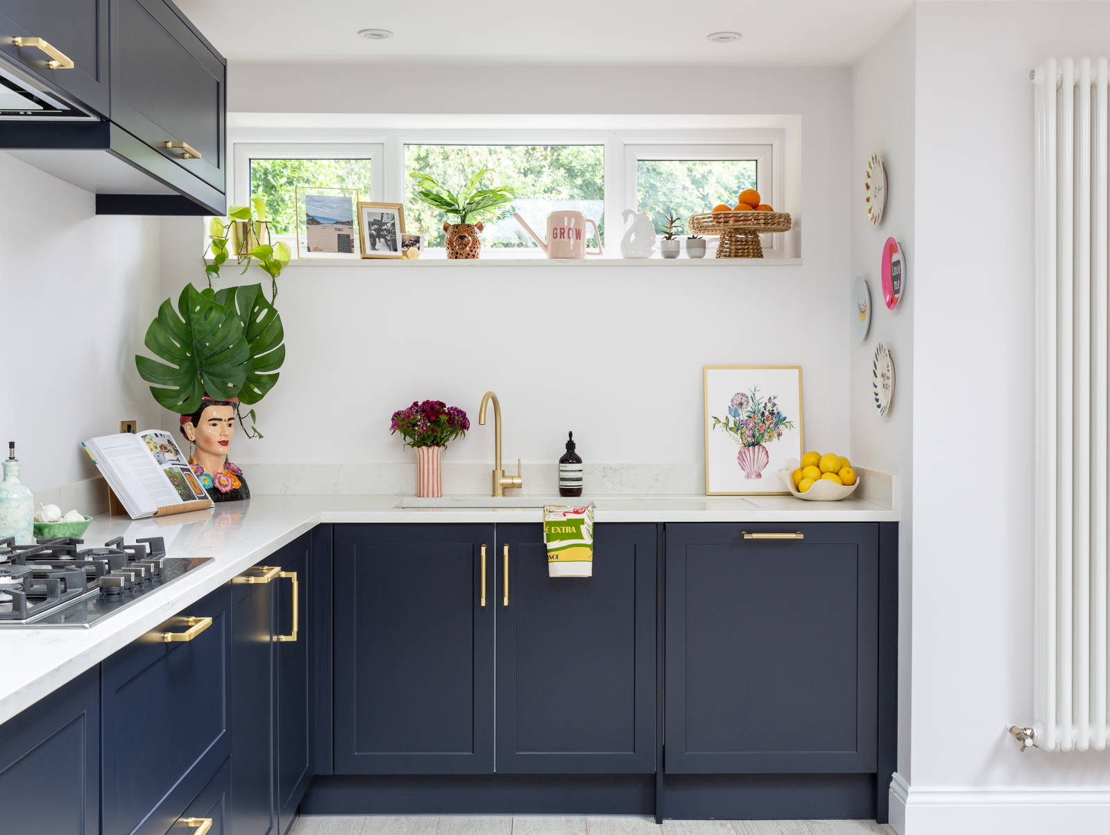 A contemporary dark blue frame kitchen with brass handles and tap. Decorated with colourful and lively pots and plats.