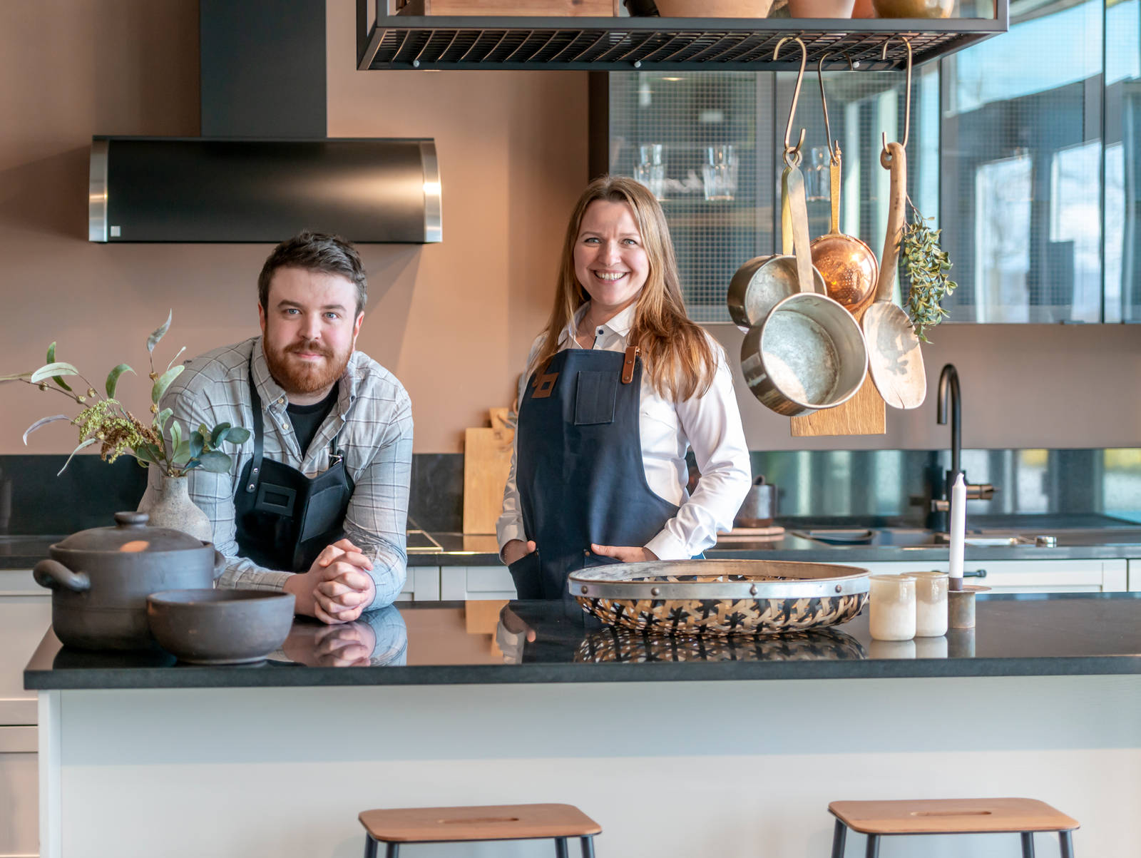 Kjøkkendesignere iført skjorter og blå forklær smiler til kameraet utenfor Sigdals butikk