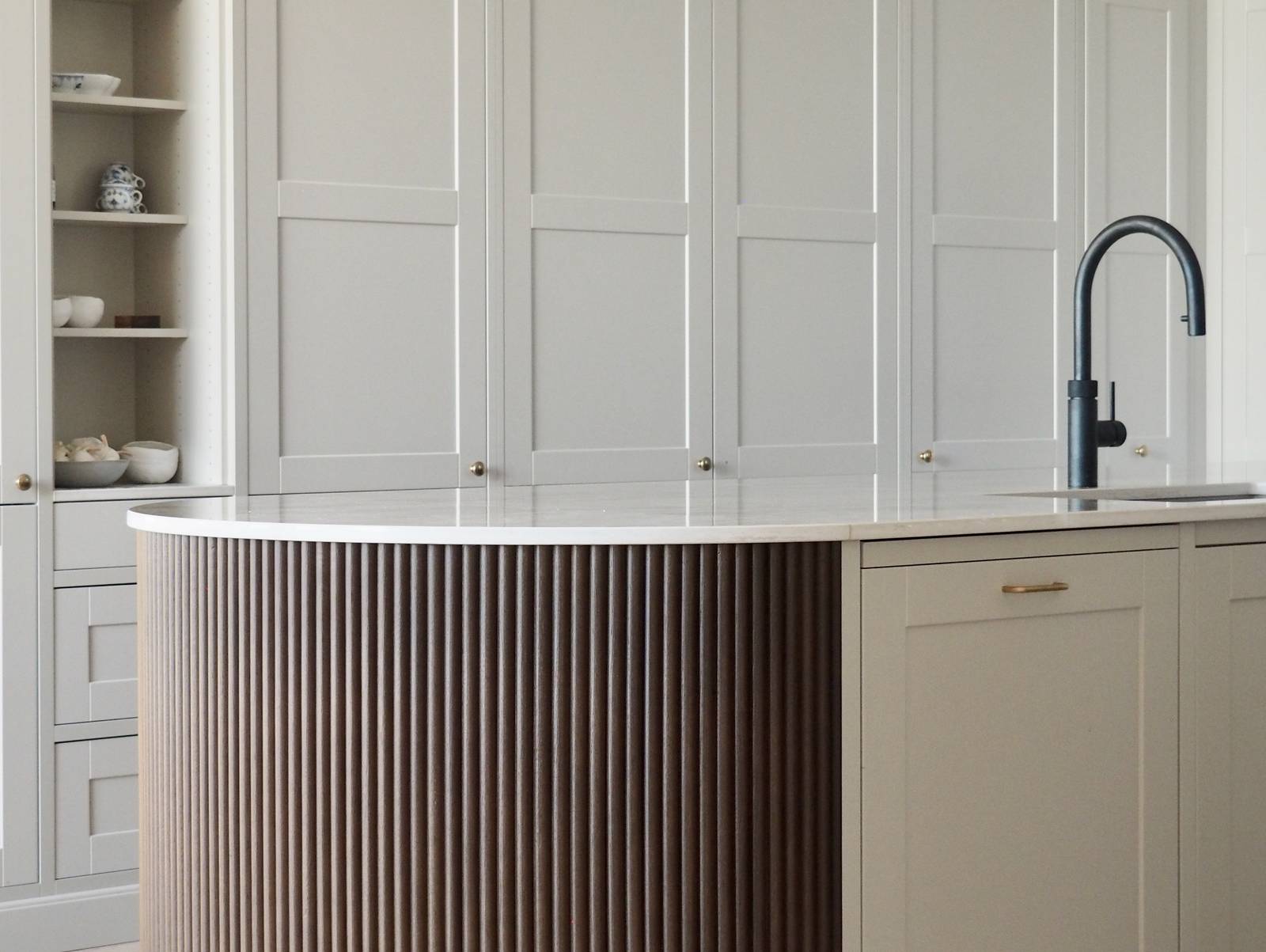 Enden af ​​den afrundede køkkenø med mørkt træpanel, Dekton Taga bordplade og sorte barstole