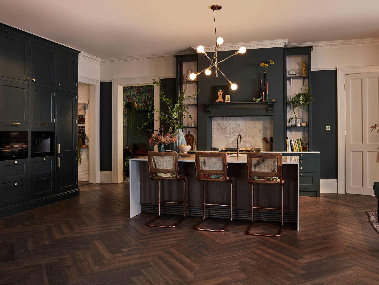 Ludlow Arboretum Green kitchen with wall cabinets and matching open shelves, bar stools by kitchen island, oven and coffee machine in tall cabinets