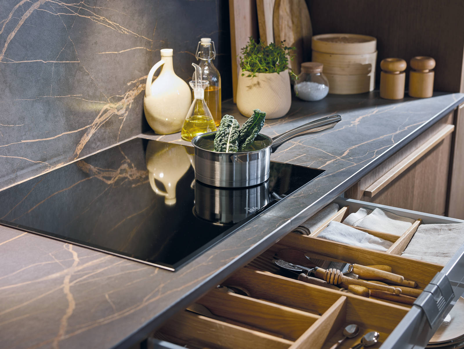 Induction hob on marbled worktop, matching backsplash, and an opened drawer with oak inserts