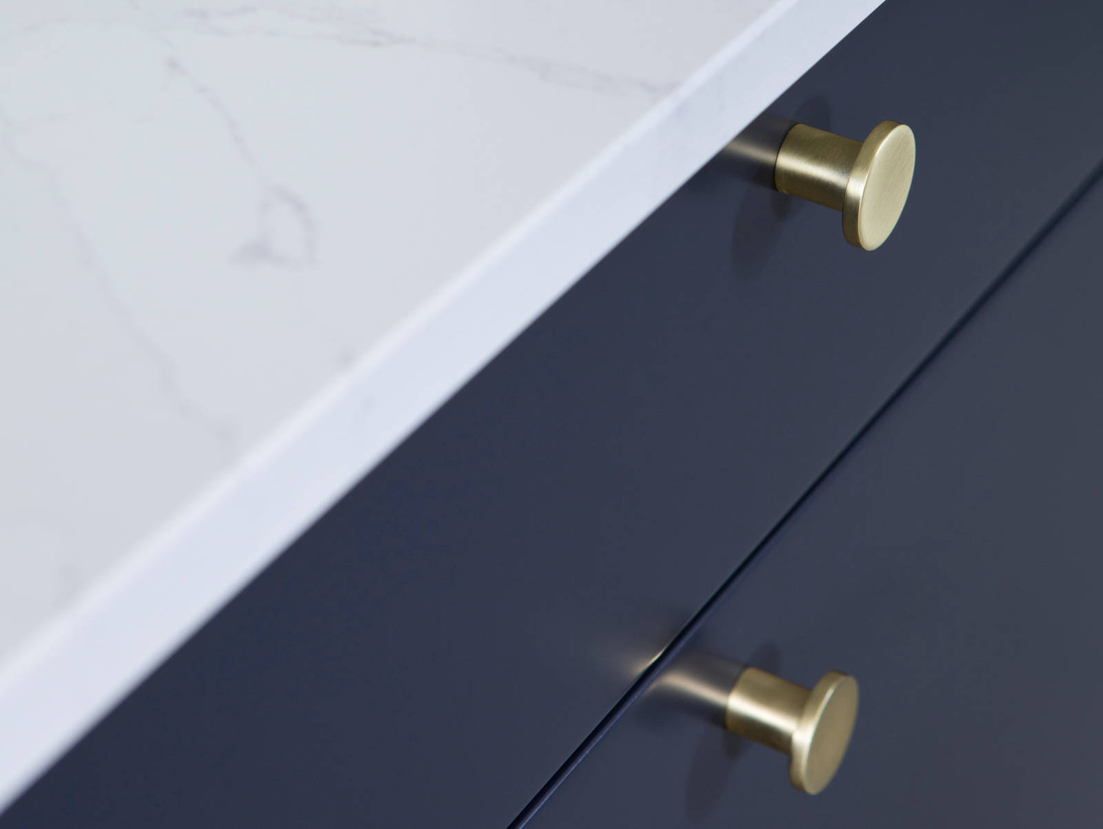 Lähikuva messinkinupeista tummansinisissä Meri keittiön laatikoissa, joissa on valkoinen marmoroitu työtaso