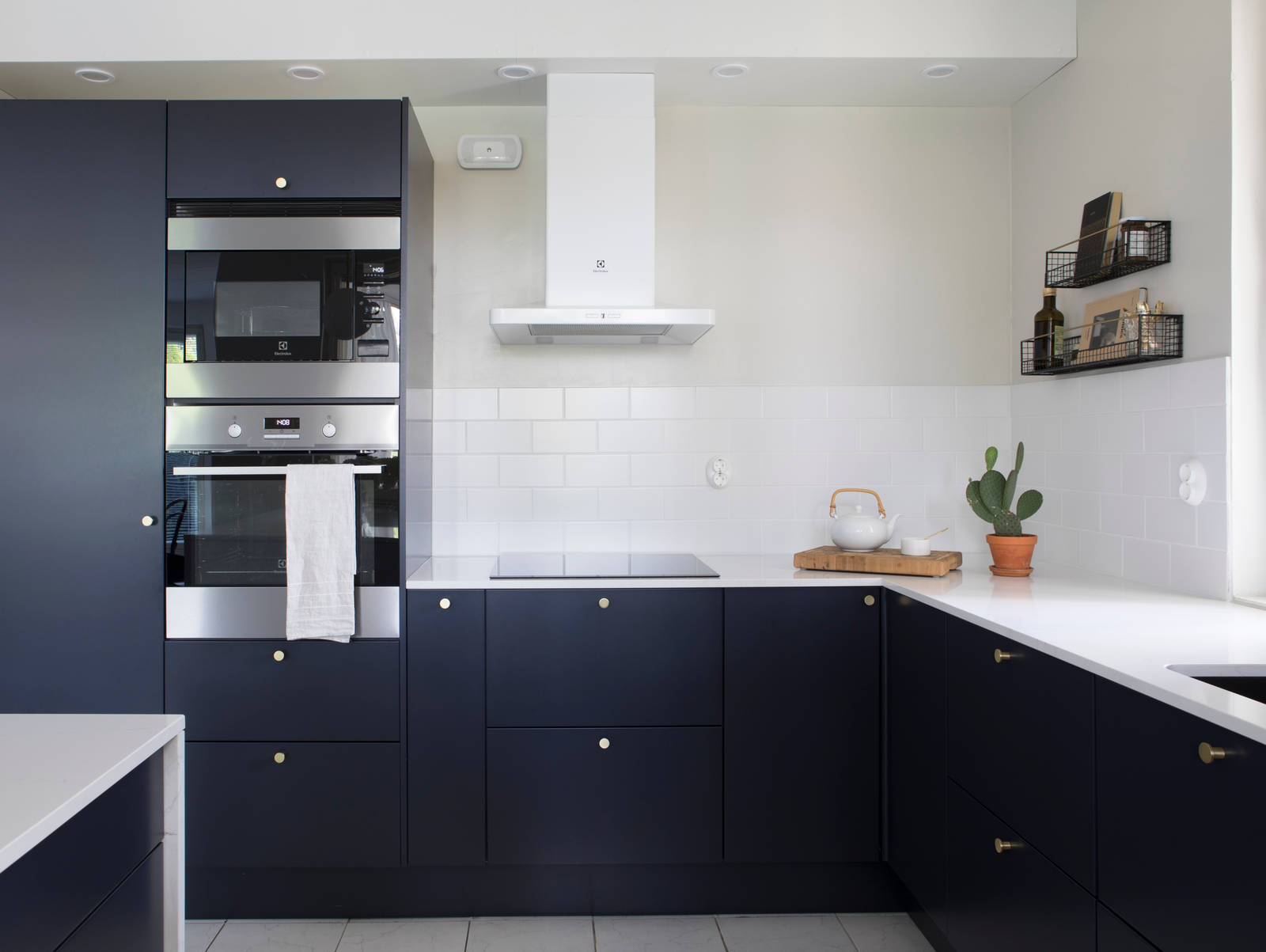 Tummansiniseksi Meri maalattu sileä keittiö, jossa valkoinen marmoroitu työtaso ja yhteensopivat splashback, messinkinupit