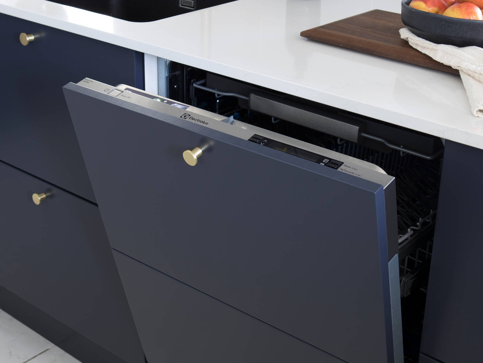 Lähikuva integroidusta astianpesukoneesta tummansinisessä Meri -maalatussa sileässä keittiössä, jossa on valkoinen marmoroitu työtaso ja messinkinupit