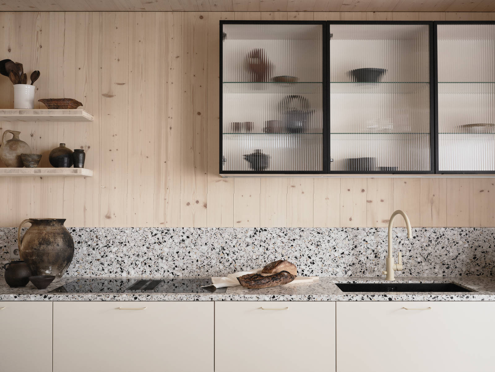 Beige blandare och svart diskho i terrazzo-bänkskiva med matchande stänkskydd, vitrinskåp med räfflat glas i Edd Ruchtons Grand design kök i beige Arkitekt Plus-kök från Marbodal