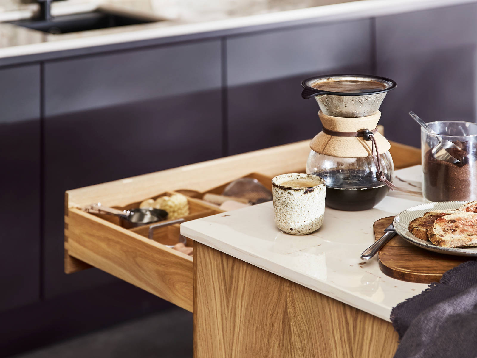 Close-up of opened oak drawer in Nordic Craft kitchen island, with breakfast served on handmade ceramics on the worktop.