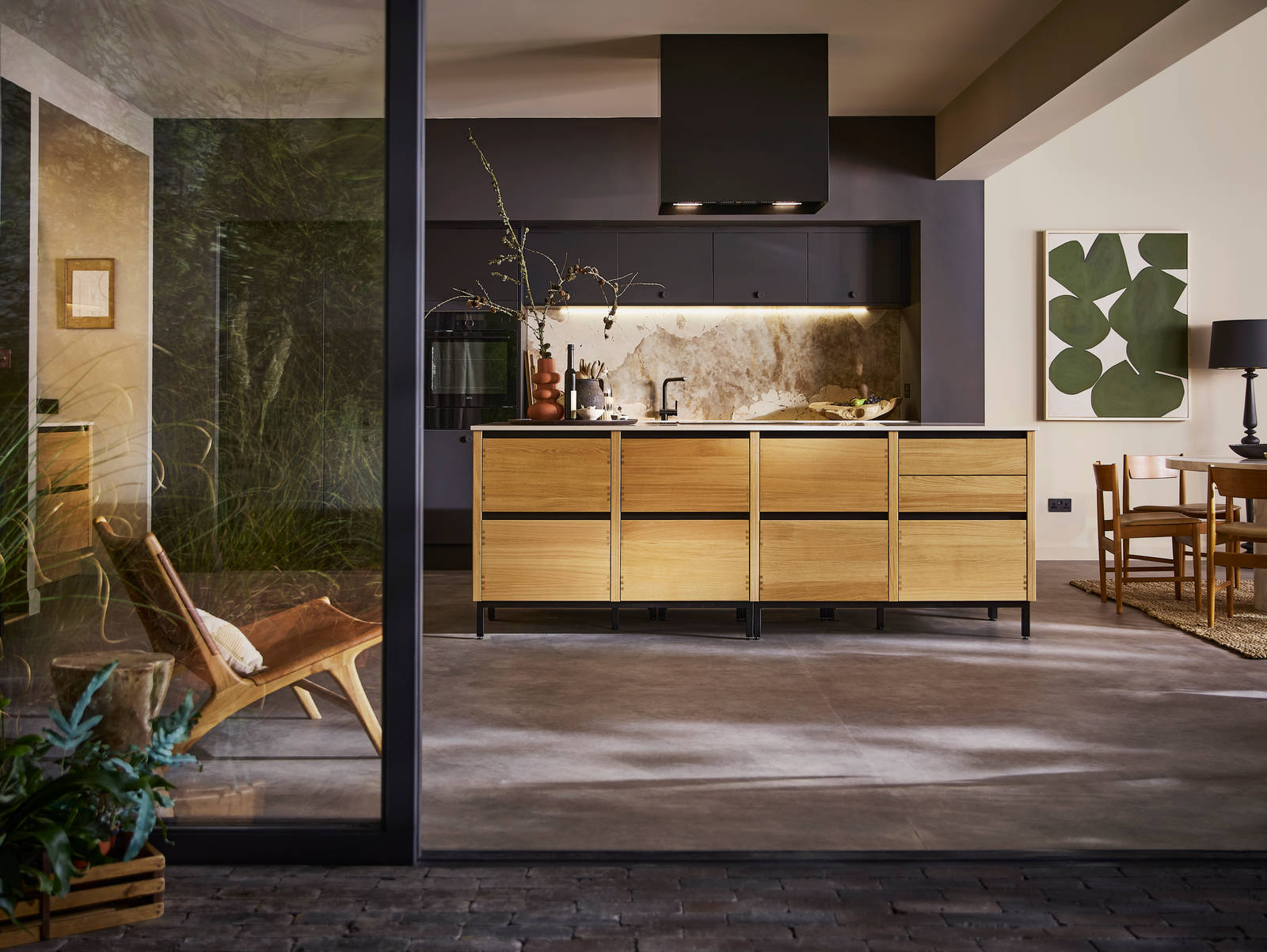 Open floorplan kitchen Mindful World, view from outside open glass foors to patio, with kitchen table and black ceiling-mounted Roroshetta Mantica Sense.