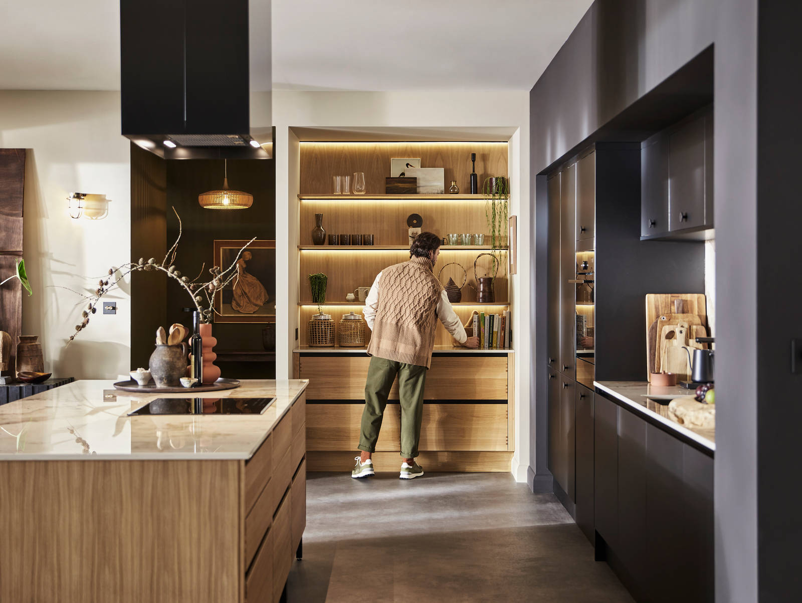 Man organising reaching for cook book in natural oak open shelves with matching wall paneling over Nordic Craft cabinetry.