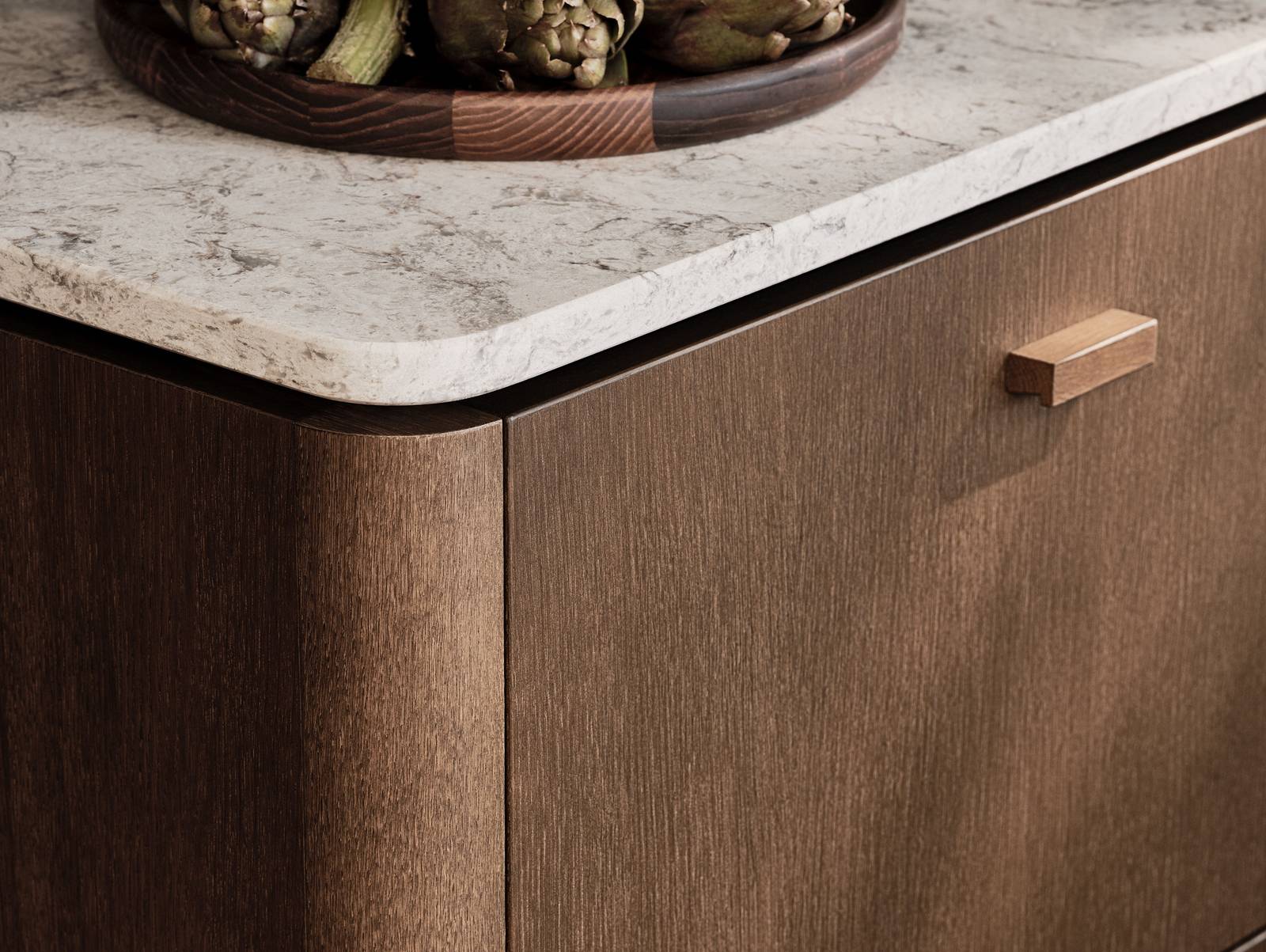 Nærbillede af afrundet hjørne på køkkenø Forever Oak fra INVITA, mørk eg køkkenskabe og håndtag med afrunded Mont Blanc Quartzite bordplade