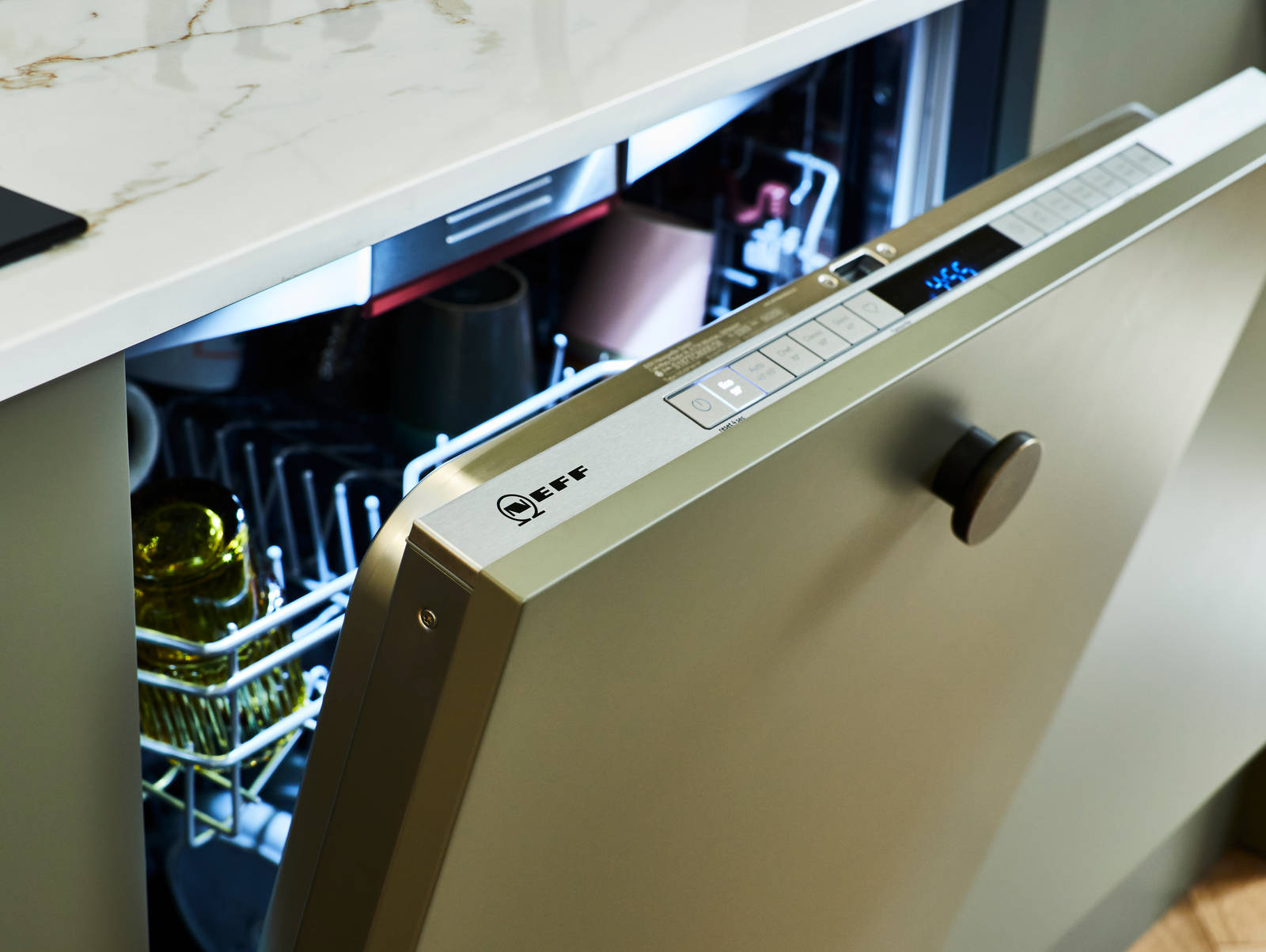 A partially open Neff dishwasher, integrated into Balmoral Green Soho cabinetry featuring a sleek white worktop and modern handle.