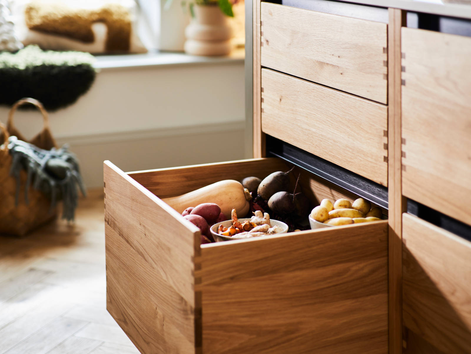 Opened large lower drawer in the kitchen island Nordic Craft cabinet, filled with fresh vegetables.