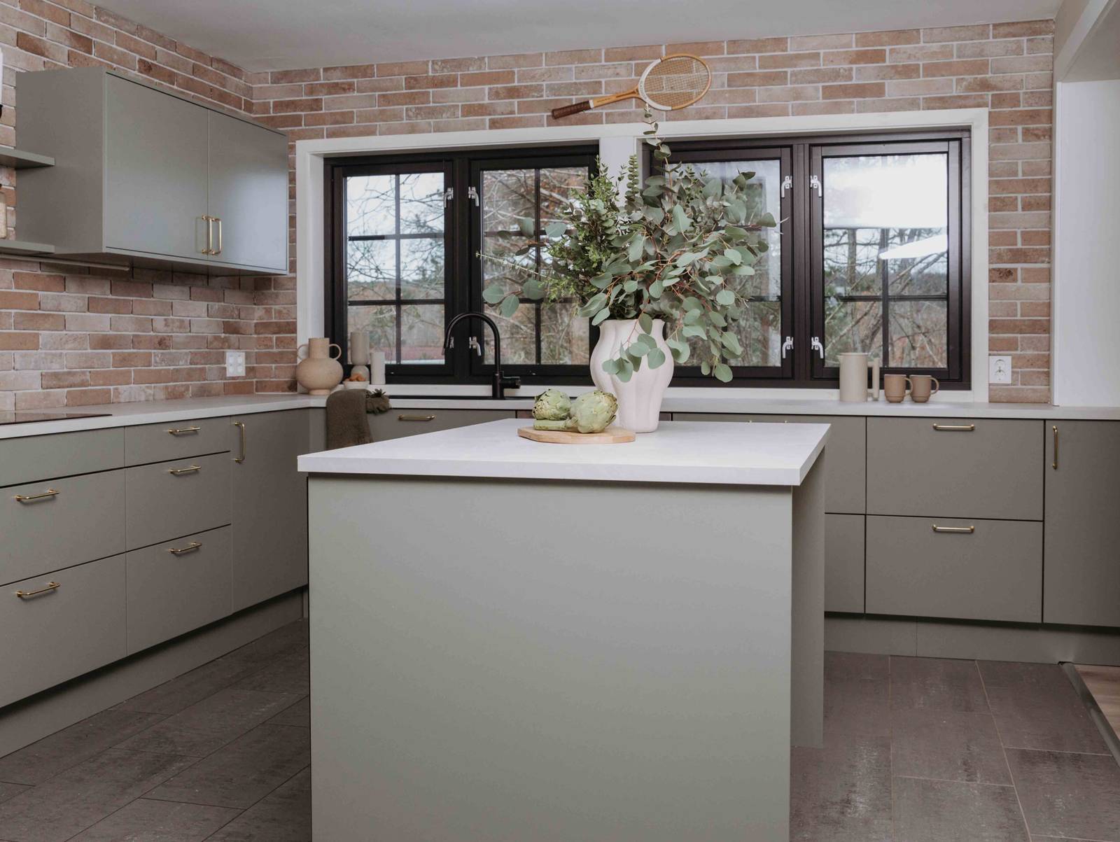 En keramikkvase med grønne planter og et skjærebrett i tre med ertebelger på kjøkkenbenken i Stine Hartmanns Uno Furu kjøkken fra Sigdal