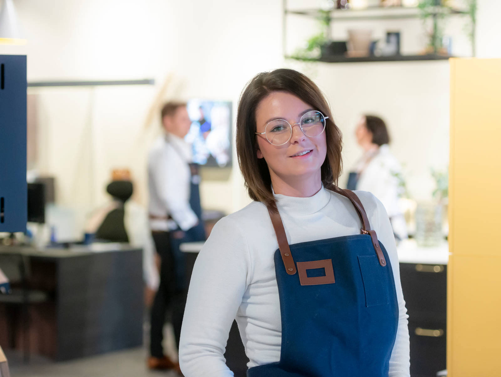Kjøkkendesigner i hvit skjorte og blått forkle smiler til kameraet utenfor Sigdals butikk