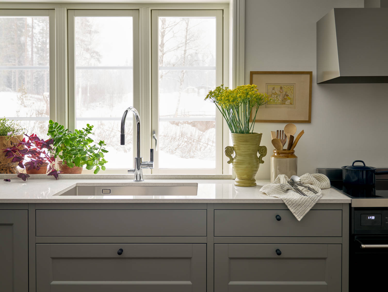 Diskho och blandare i rostfritt stål med utsikt genom stora fönster i i Malin Berghagens kök från Marbodal, lantliga Fagerö i kulören Frö med vit och grå marmorerad bänkskiva.