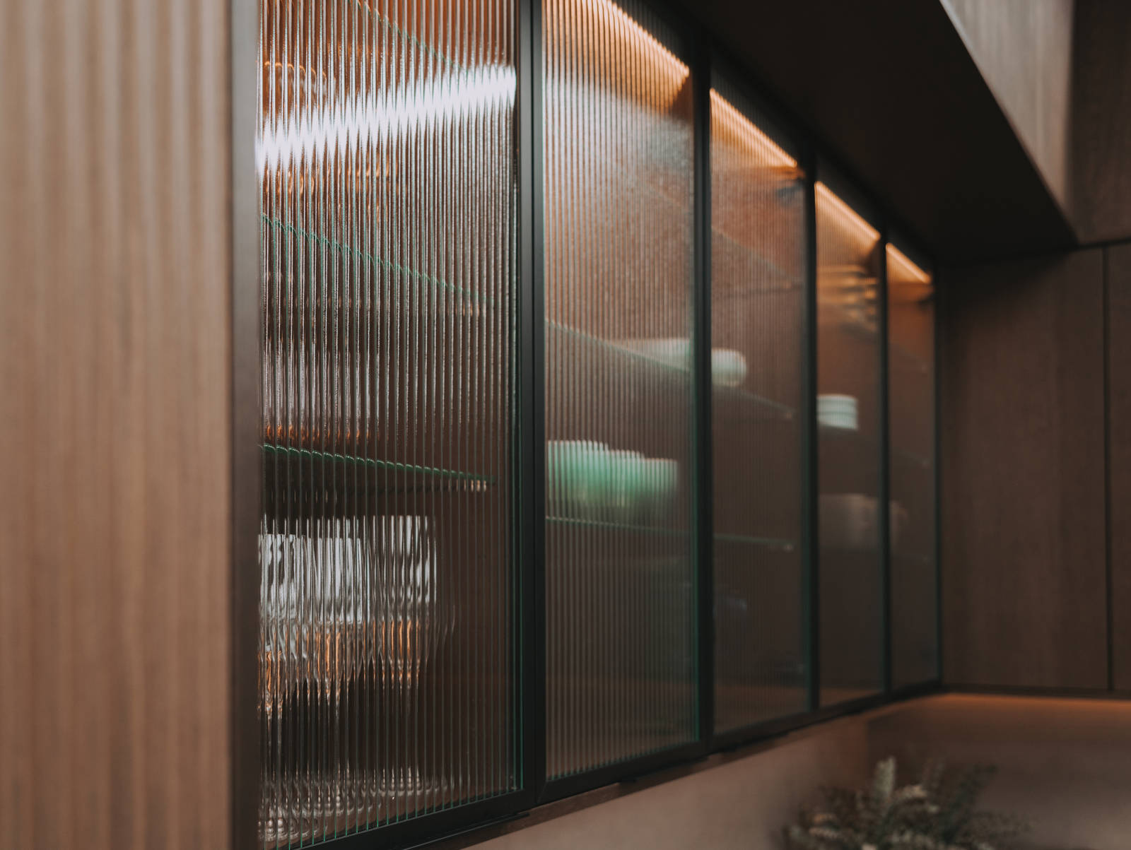 Vitrinedører med bølget glass og sorte aluminiumsrammer i kjøkkenet Favn fra Sigdal i lekker eikefinér som er beiset i fargen Nøtt, i God Morgen Norge studion sin