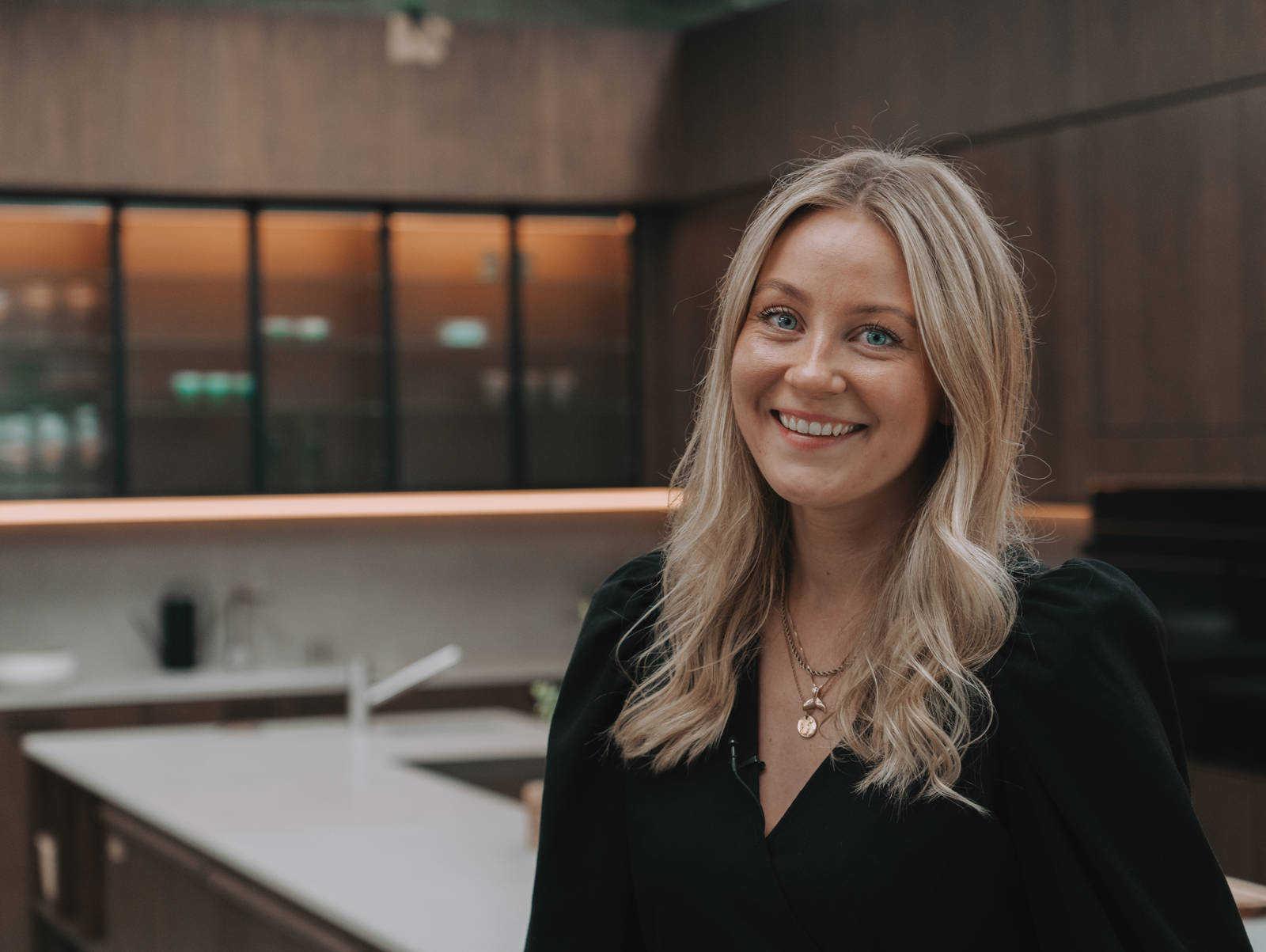 Hanna Stenseth i kjøkkenet Favn fra Sigdal i lekker eikefinér, som er beiset i fargen Nøtt, kjøkkenøya og vitrinedører med bølget glass og sorte aluminiumsrammer i God Morgen Norge studion sin