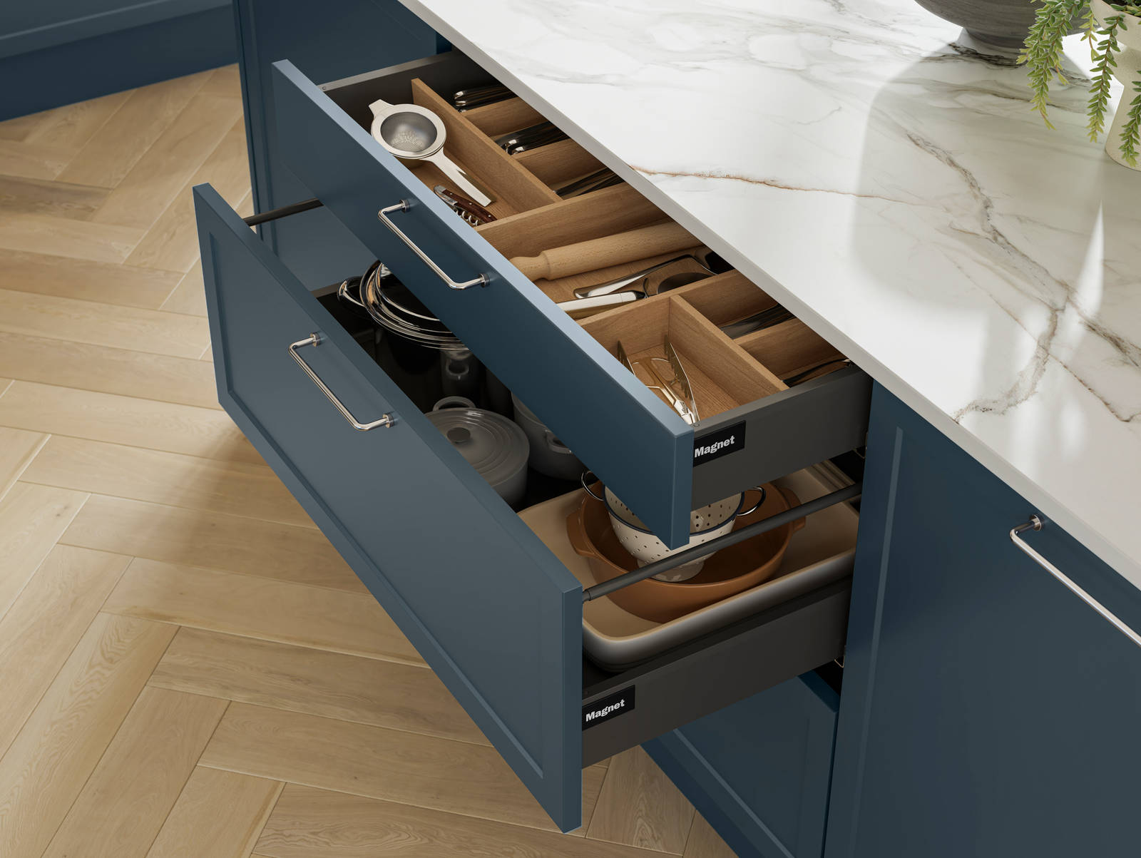 Pulled out drawers in Brunswick Voyage blue kitchen island with oak cutlery inserts, white and grey marbled worktop and light wood herringbone flooring.