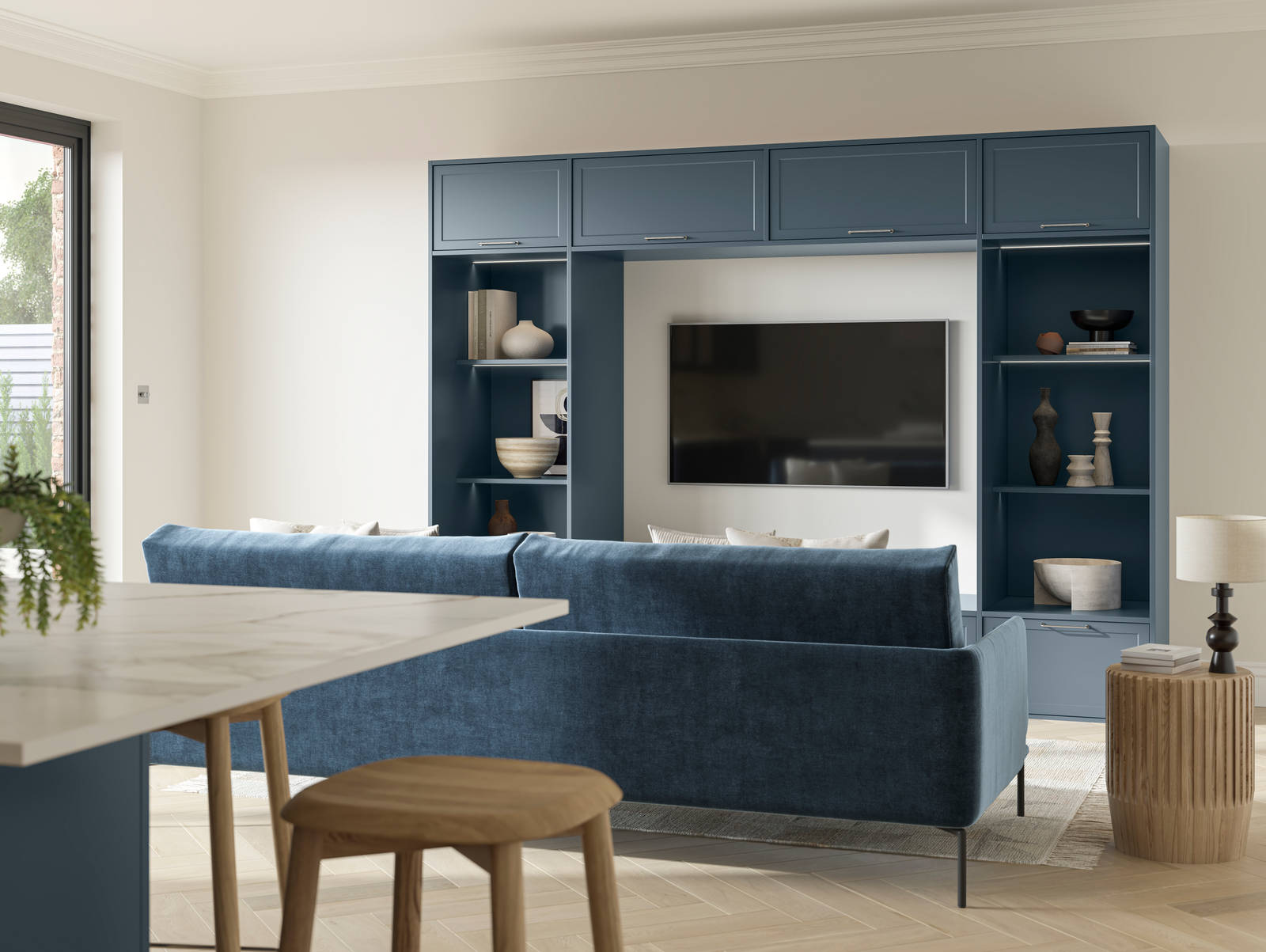 Cabinets and open shelves around a wall mounted TV in the modern Shaker range Brunswick Voyage Blue, matching blue counch and kitchen island in the foreground.
