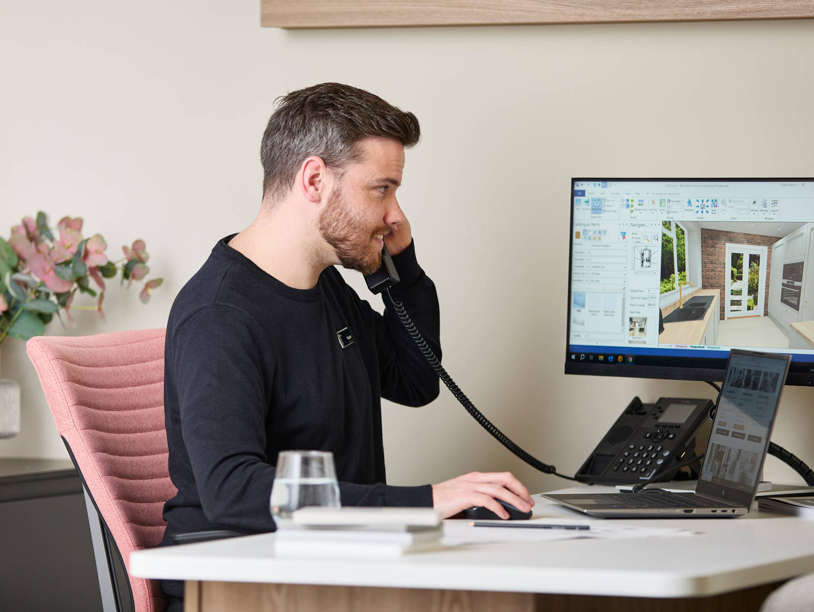 Magnet colleague at a desk, speaking on the a phone while designing a kitchen on a computer