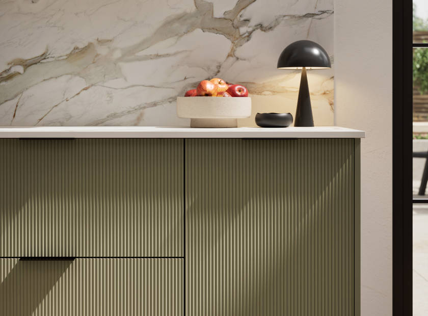 Fluted front kitchen Reed from Magnet in deep green shade Balmoral, with a marbled splashback and black handles, herringbone wood flooring.