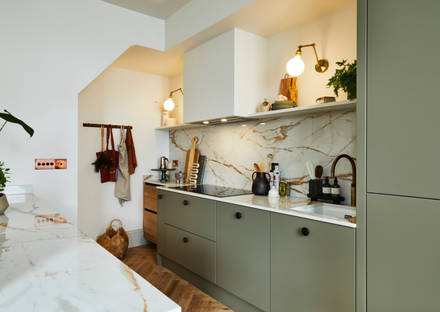 Modern slab Soho Balmoral cabinet paired with modern appliances, a marbled worktop and backsplash, brass details and plants.