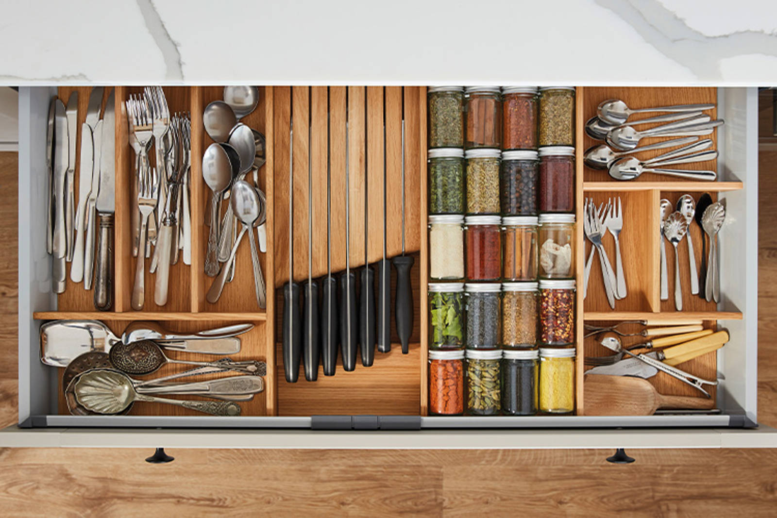 Opened drawer with oak inserts for cutlery, jars of spices and knives.