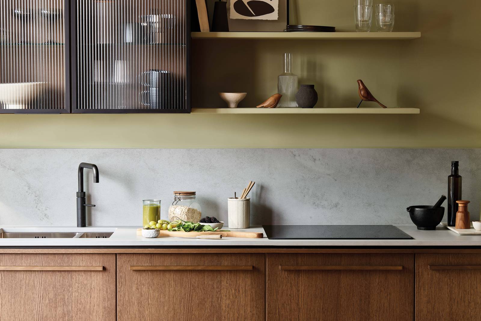 Fluted glass wall cabinets in a Nordic Nature oak kitchen, a grey worktop, matching backsplash and black tap.