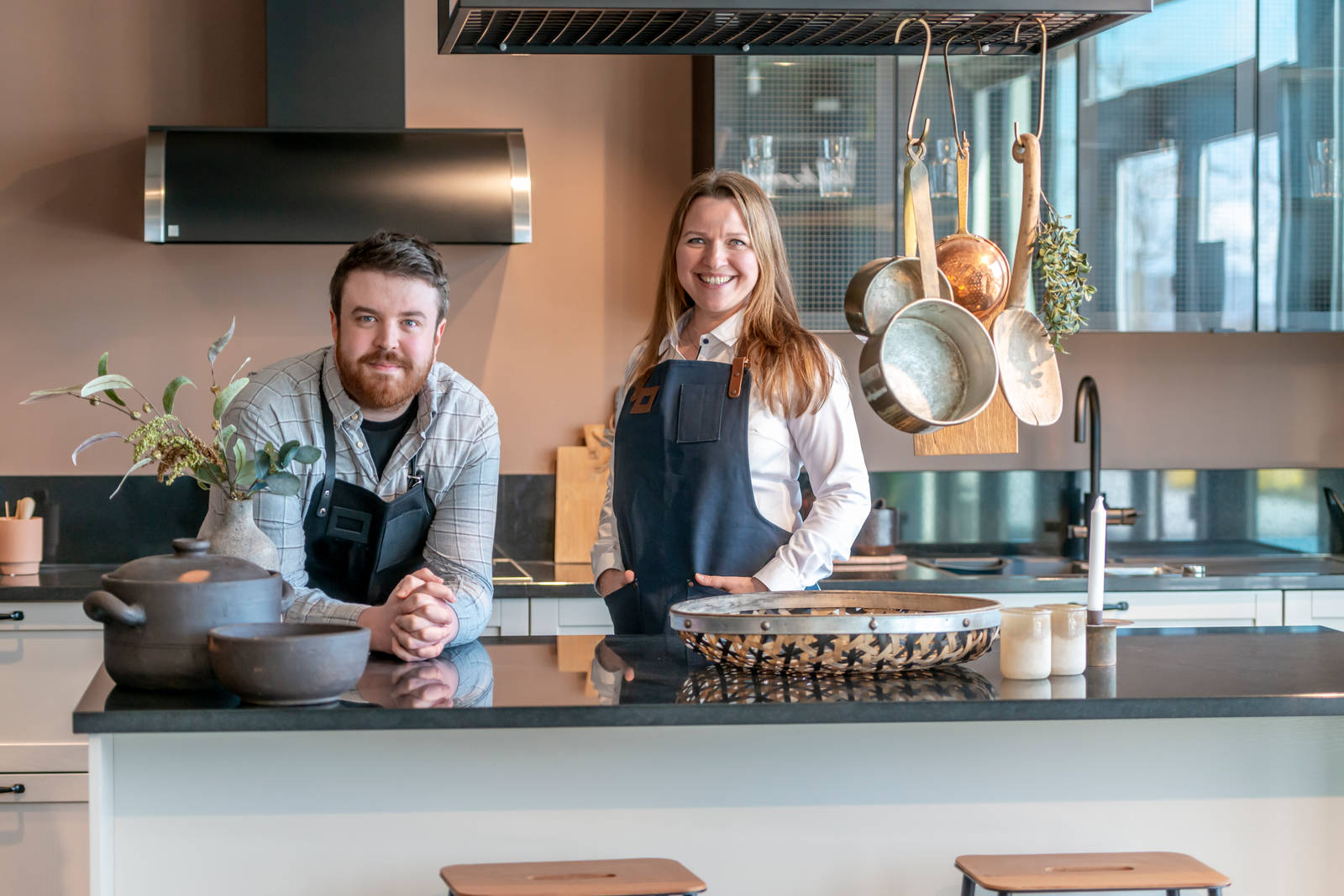 Kjøkkendesignere iført skjorter og blå forklær smiler til kameraet utenfor Sigdals butikk