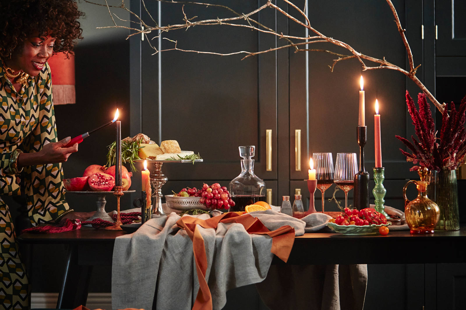 Opulent table setting with lit candles in mixed colours, cheese and pommegranates in Ludlow Arboretum kitchen from Magnet.