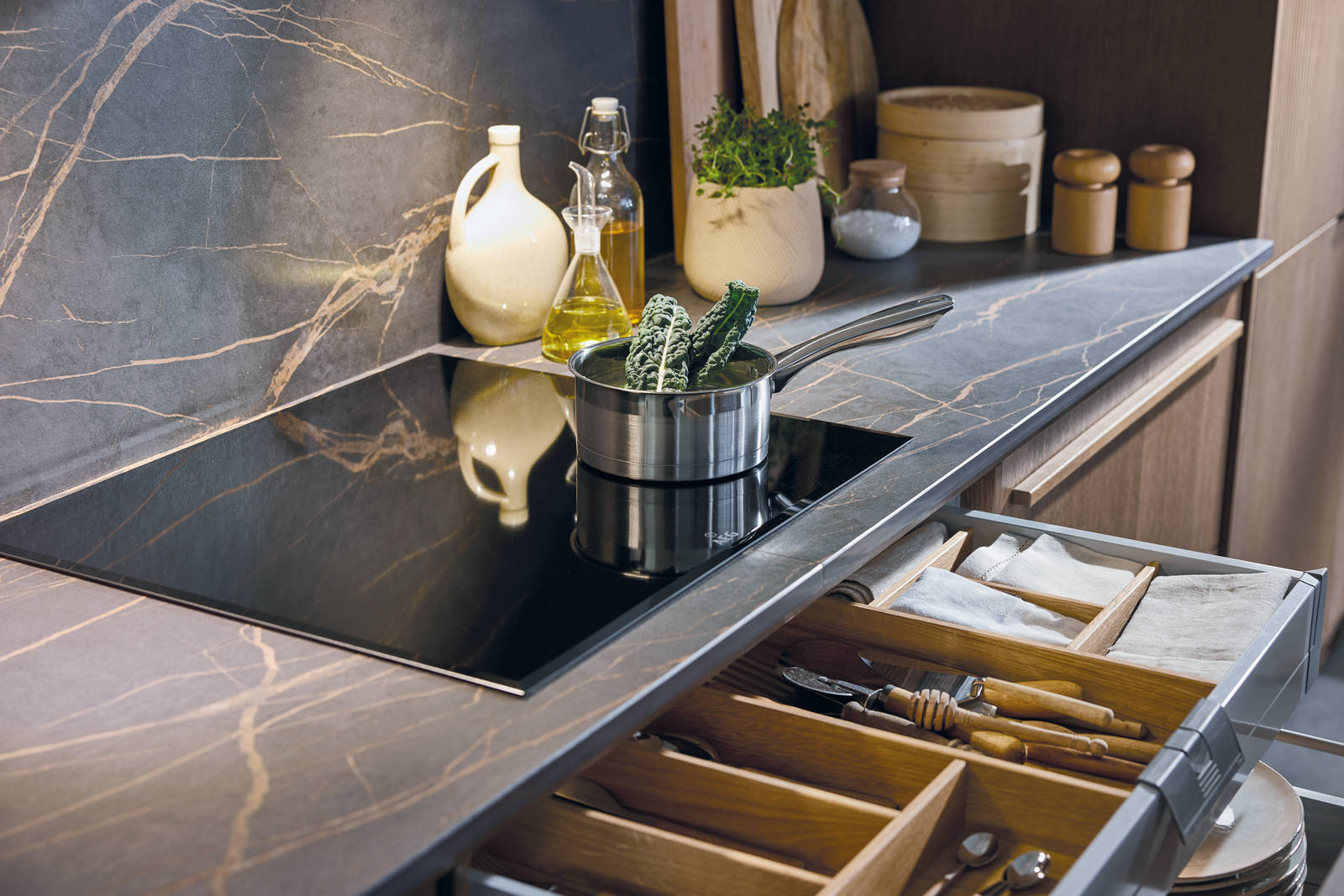 Induction hob on marbled worktop, matching backsplash, and an opened drawer with oak inserts