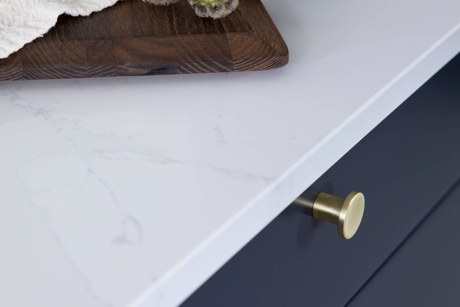 Lähikuva messinkinupeista tummansinisissä Meri keittiön laatikoissa, joissa on valkoinen marmoroitu työtaso