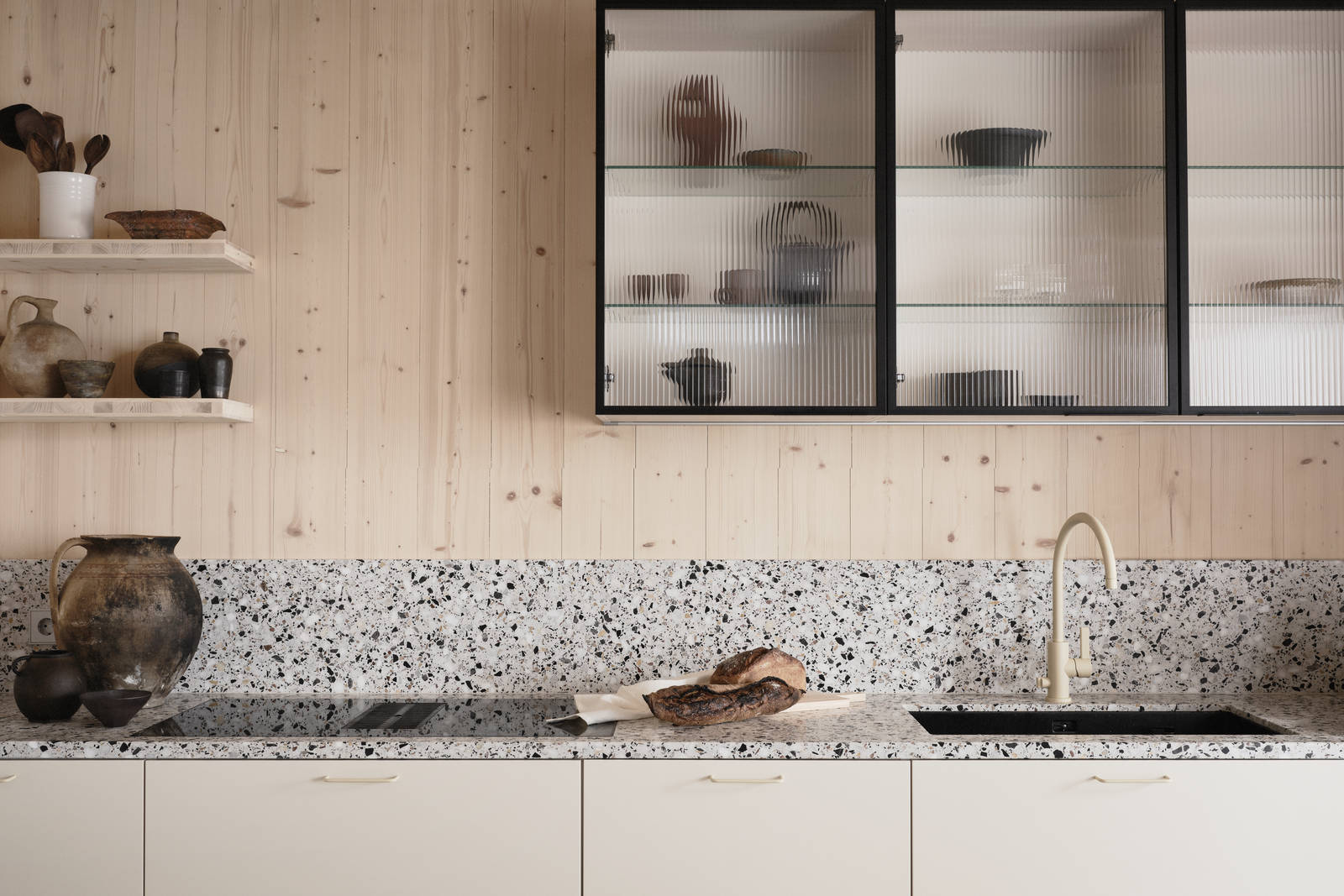 Beige blandare och svart diskho i terrazzo-bänkskiva med matchande stänkskydd, vitrinskåp med räfflat glas i Edd Ruchtons Grand design kök i beige Arkitekt Plus-kök från Marbodal