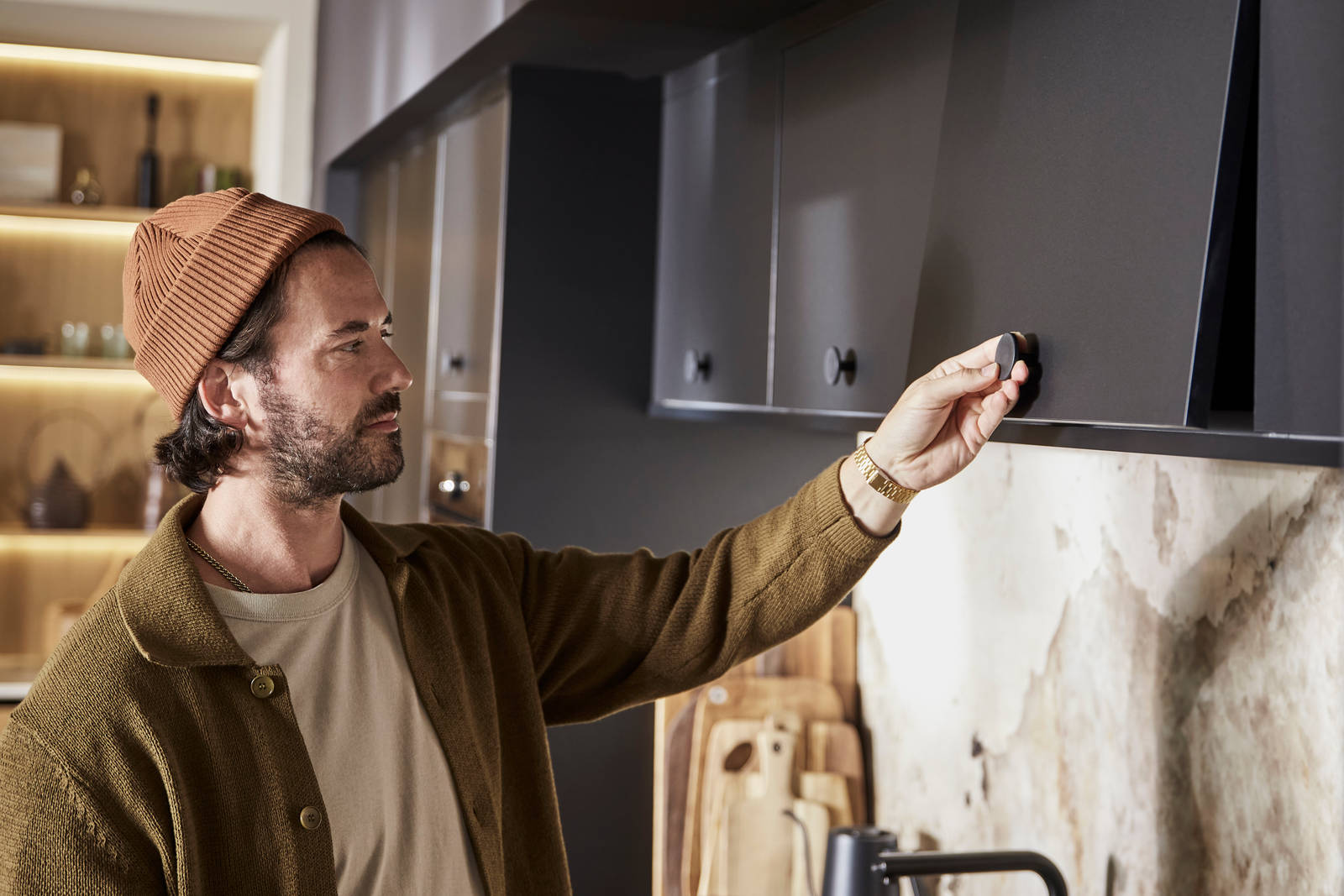 Man wearing clothes in earth tones opening a top cabinet in Hoxton Sumi Black
