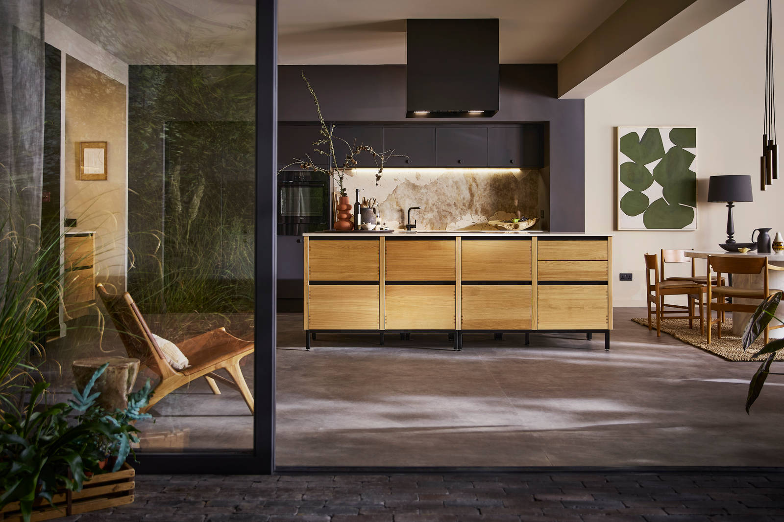 Open floorplan kitchen Mindful World, view from outside open glass foors to patio, with kitchen table and black ceiling-mounted Roroshetta Mantica Sense.